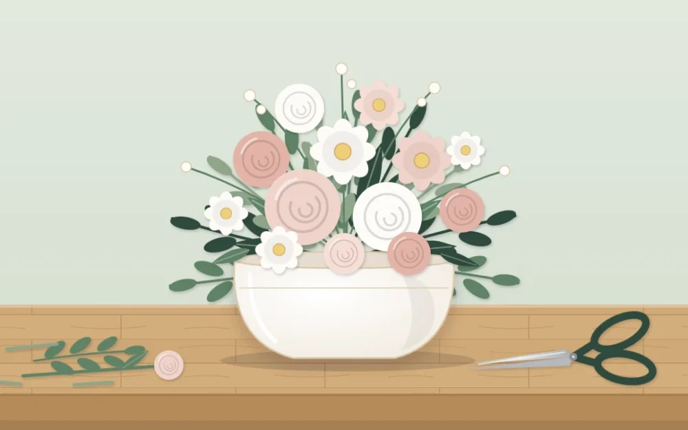 Low, wide ivory ceramic vase on a wooden tabletop holding a rounded arrangement of blush and white flowers with leafy greenery, cut stems and scissors beside it