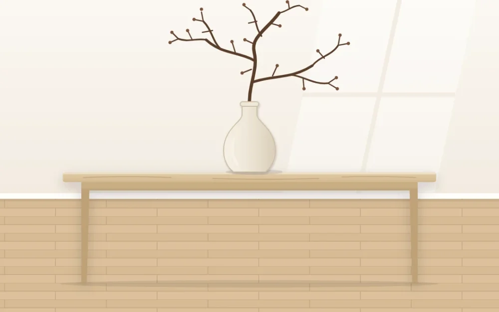 Side view of a pale oak table against an empty warm white wall with one matte ivory vase holding a single bare branch