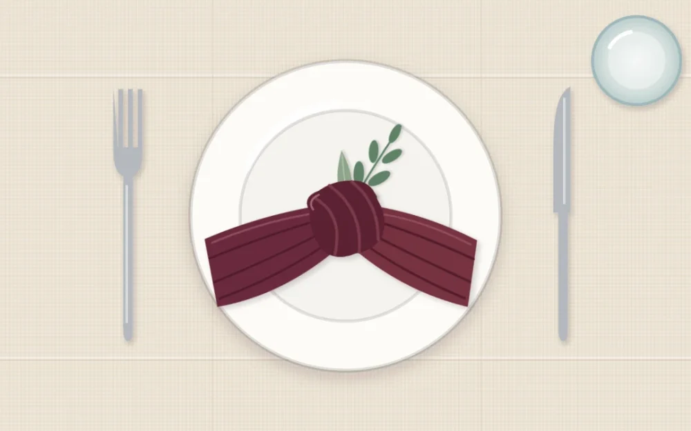 Top-down view of an ivory plate with a wine-colored cloth napkin tied in a loose knot and a small green sprig, fork to the left and knife to the right