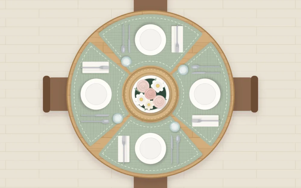 Top-down round wooden table set for four with wedge placemats, ivory plates and napkins, and a low bowl of flowers in the exact center
